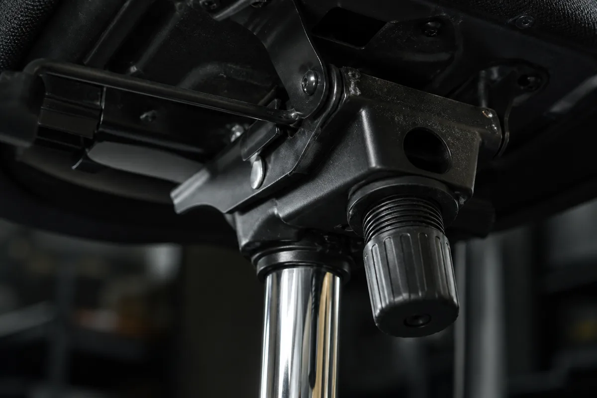 Détail du mécanisme synchrone et du vérin à gaz sous l&rsquo;assise d&rsquo;un siège de bureau, lumière rasante sur le métal